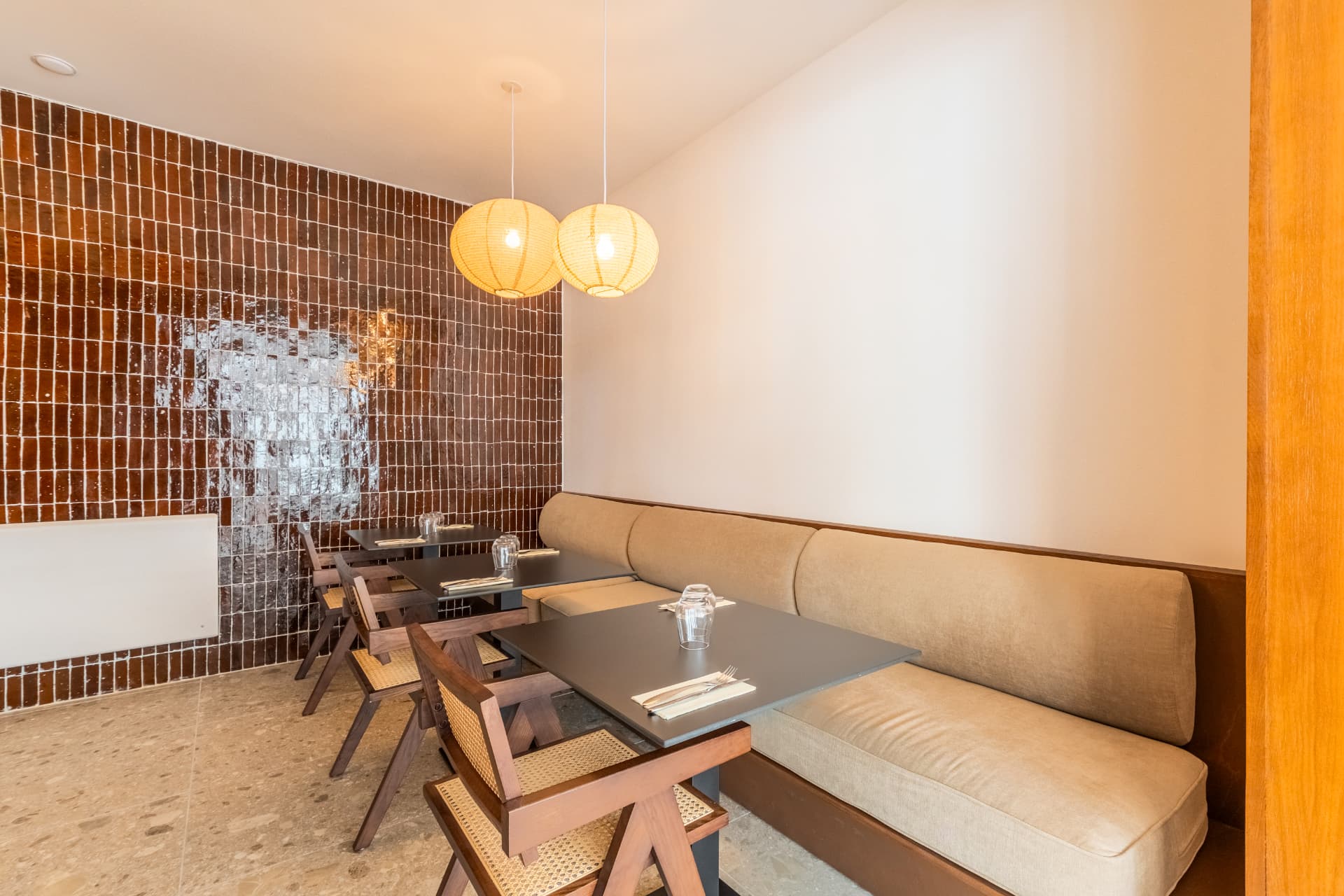 Banquette d'angle et tables noires sous des lanternes chaudes