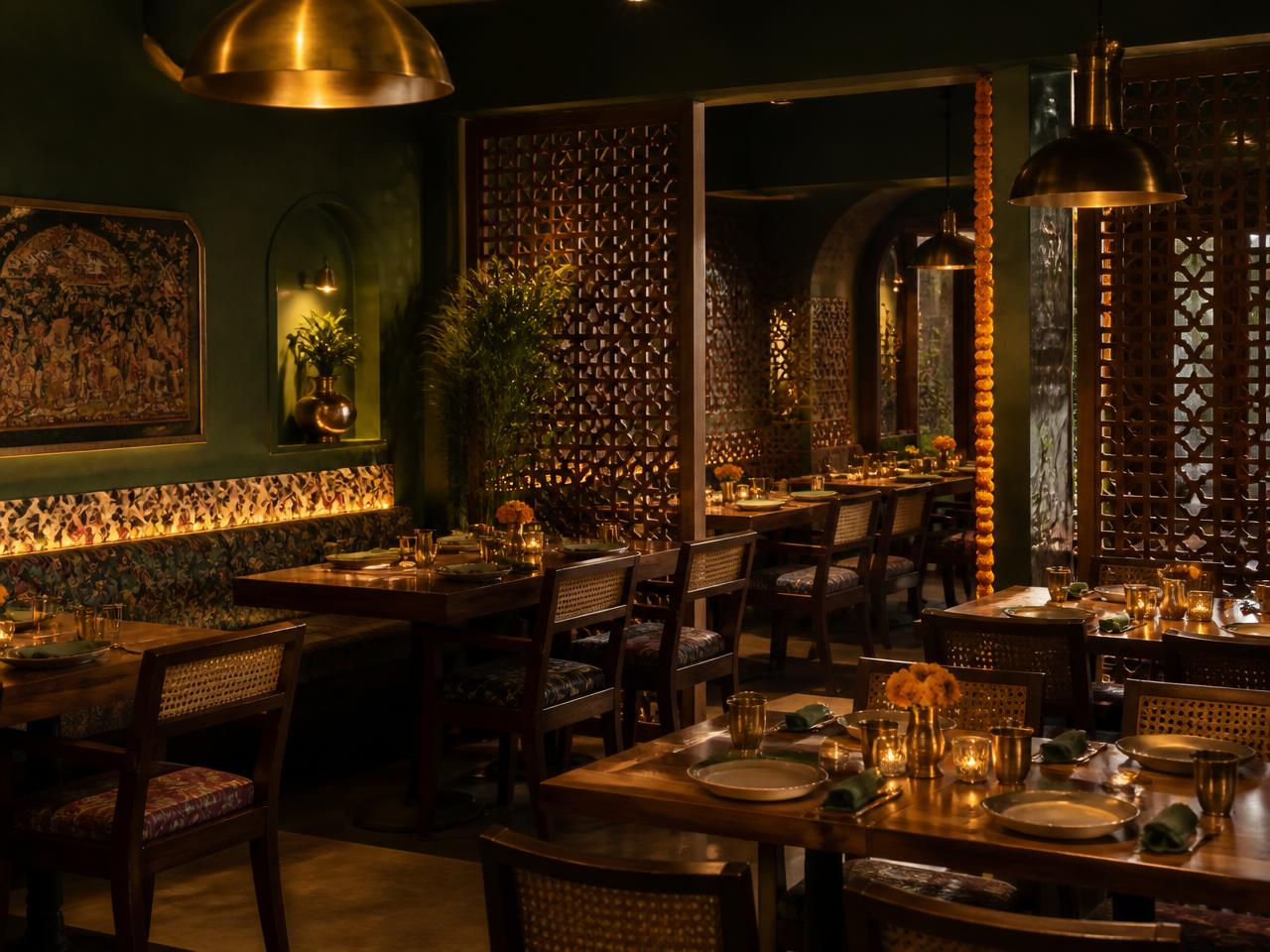 Salle du restaurant Dhamaka avec murs verts, lampes en laiton et claustras en bois